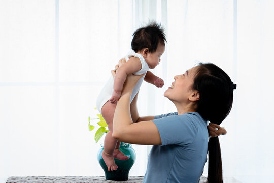 Asian single mom, holding up his daughter, The mother held her daughter up to tease her, and she kissed her nose on her cheek, The daughter looked at her mother, and smiled at her joyfully.