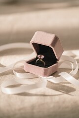 Vertical shot of a pink diamond ring in a velvet box and ribbon on a burlap mat