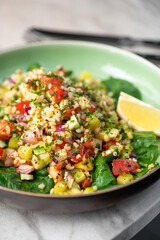 Tabbouleh salad with bulgur, tomatoes, parsley, green onion and mint in plate on grey stone table. Traditional middle eastern or arab dish.