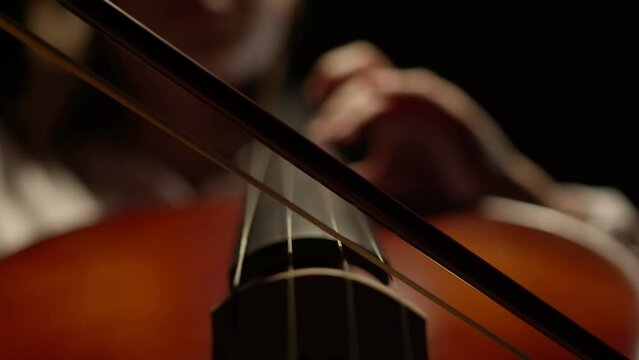 Young person in white shirt playing classical music on a cello, musical string instrument of the violin family. Closeup shot of cellist hand holding cello bow during orchestra concert or rehearsal