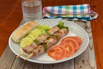 Plato de brochetas de pavo con tomate y lechuga y un vaso de agua, sobre la mesa