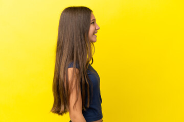 Little caucasian girl isolated on yellow background laughing in lateral position