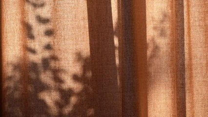 Beautiful linen curtains reflect the shadows of the branches and leaves of the trees outside on a sunny morning.