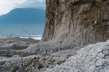 Fototapeta na wymiar cloudy rocky seashore formed by columnar basalt against the backdrop of a stormy sea, coastal landscape of the Kuril Islands