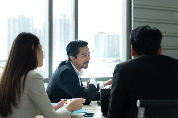 A group of young Asian entrepreneurs. Top Management is meeting to review stock investment data from the team in a meeting room with natural light