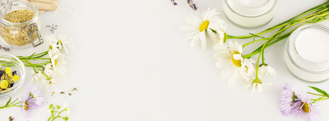 Natural products from wild plants and flowers. Eco friendly banner with natural flowers and herbs, tea bags, jars with cream on a white background with copy space. Banner size - obrazy, fototapety, plakaty