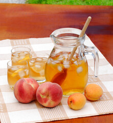Peach cold tea jar ice glasses and peach fruits on outdoors table background.