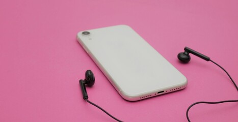 Smartphone with headphones on a pink background. Listen to music, copy space