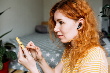 Happy red-haired girl listening music, at home in wireless headphones