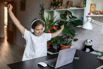 girl of primary school age of European appearance does homework, takes notes in headphones with a laptop at home. Concept Back to school, School distance education at home, home schooling, e-learning