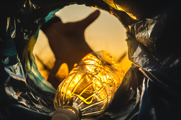 Close-up of a hand throwing a plastic bottle into the trash can. Close-up of the inside of a garbage can in the rays of the setting sun