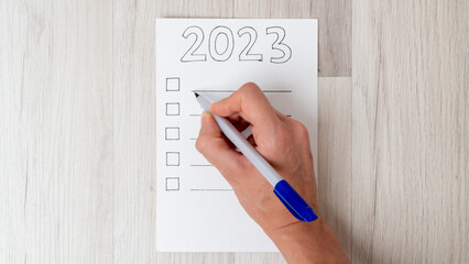 A woman's hand fills the checklist with a pen for the new year 2023