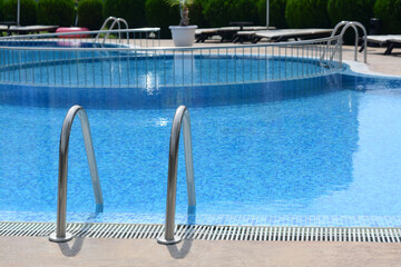 Outdoor swimming pool with ladder and handrails on sunny day, space for text