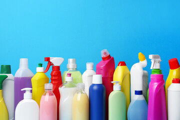 Many bottles of different detergents on light blue background. Cleaning supplies