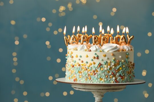 Beautiful birthday cake with burning candles on stand against festive lights. Space for text