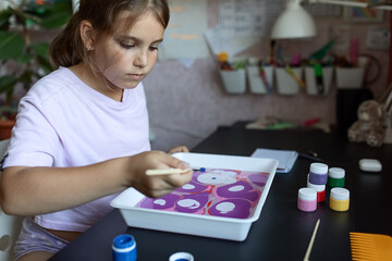 an attractive girl of primary school age of European appearance paints on the water in the ebru technique. The concept of children's creativity