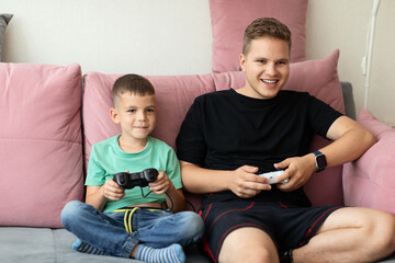 Two brothers with joysticks in their hands are playing computer games comfortably sitting on the couch at home. online games with friends, selective focus