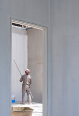 Asian builder worker using long handle roller brush to applying primer white paint on concrete wall...