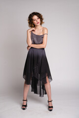 High fashion photo of a beautiful elegant young woman in a pretty dark gray dress, hairstyle on white, soft gray background. Studio Shot. 