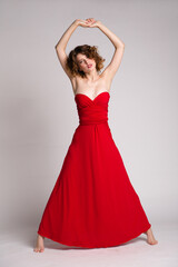 Naklejka premium High fashion photo of a beautiful elegant young woman in a pretty long red dress, hairstyle on white, soft gray background. Studio Shot. 