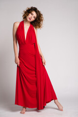 High fashion photo of a beautiful elegant young woman in a pretty long red dress, hairstyle on white, soft gray background. Studio Shot. 
