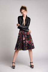 Fototapeta premium High fashion photo of a beautiful elegant young woman in a pretty dark long skirt with floral pattern, black leather jacket on white, soft gray background. Studio Shot. 
