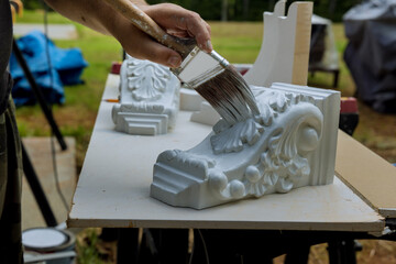With a paintbrush, worker paints wooden corbels for kitchen island on table surface © ungvar