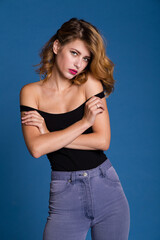High fashion photo of a beautiful elegant young woman in a pretty black sleeveless top, denim jeans, hairstyle on blue background. Studio Shot. 