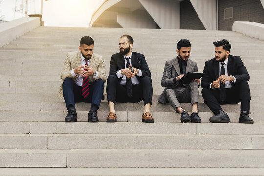 Business people outdoor meeting. A company of male businessmen in suits are sitting on the steps of the stairs. Working break. Discussion and conversation.