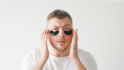 Skincare procedure. Facial treatment. Morning routine. Metrosexual man applying hydrogel black under eye patches on light background.