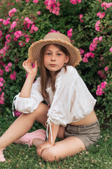 Cute little girl with blond hair in a straw hat. Pink flowers. Summer.