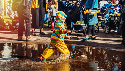 A small child in bright clothes runs through a puddle
