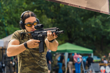 muscular Caucasian man looking through a rifle loupe at the shooting range, medium shot. High...