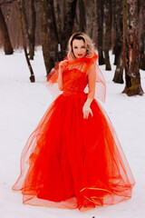 Fototapeta premium Beautiful woman in a luxurious red fairy-tale dress in a snowy forest