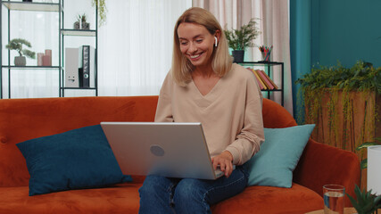 Portrait of caucasian girl sitting on couch, looking at camera, making video webcam conference call with friends or family, enjoying pleasant conversation. Young woman laughing, waving hello at home