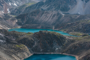Beautiful group of azure and turquoise mountain lakes at various heights among black rocks in bright sun. Two blue alpine lakes at different highs among sunlit black green rocky hills in highlands.