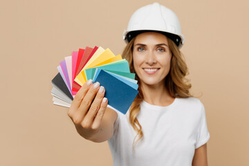 Young employee laborer handyman woman in white t-shirt helmet give close up wallpapares swatch palette isolated on plain beige background Instruments accessories for renovation room Repair concept.