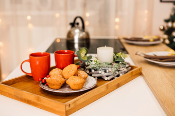 On the table is a plate of muffins, two red cups and a candle. New Year