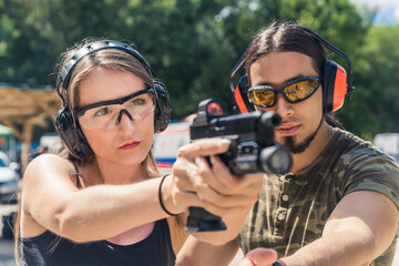 male instructor and girl with headphones and eyeglasses learning using of a pistol at the outdoor range, medium closeup. High quality photo