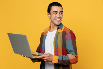 Young happy smiling middle eastern IT man wear casual shirt white t-shirt IT woman hold use work on laptop pc computer look aside isolated on plain yellow background studio People lifestyle concept.