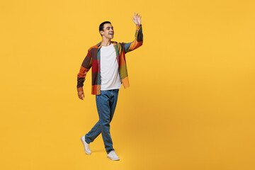 Full body side view young smiling happy middle eastern man 20s wear casual shirt white t-shirt walking going strolling waving hand isolated on plain yellow background studio People lifestyle concept.