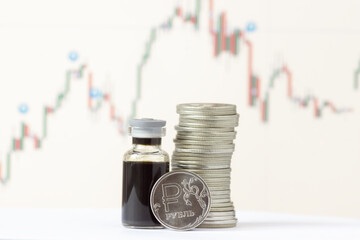Ruble coins and a bottle of crude oil against the background of a price chart. The inscription on the coin - ruble