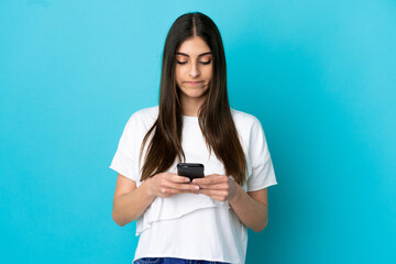 Young caucasian woman isolated on blue background using mobile phone