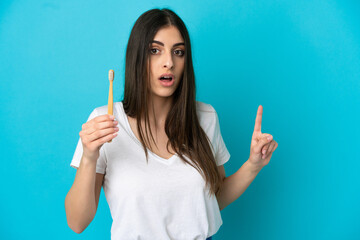Young caucasian woman brushing teeth isolated on blue background surprised and pointing side