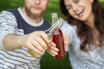 A young man and woman drink drinks in glass bottles at a picnic.