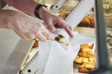 Close-up of a person's hands holding pastry tongs picking up a sweet pastry cake and putting it in...