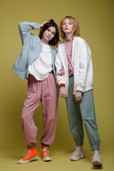 High fashion photo of a beautiful elegant young women in a pretty white, pink and green mint sports suit oversize, jacket, walking style, posing over yellow background. Studio Shot. Portrait.