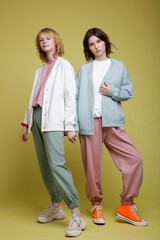 High fashion photo of a beautiful elegant young women in a pretty white, pink and green mint sports suit oversize, jacket, walking style, posing over yellow background. Studio Shot. Portrait.