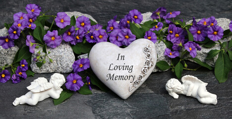 Stone heart with the lettering in Loving Memory with flowers and grave angels.