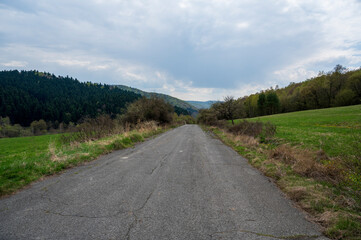 Old and empty asphalt road in the forest with a meadow.